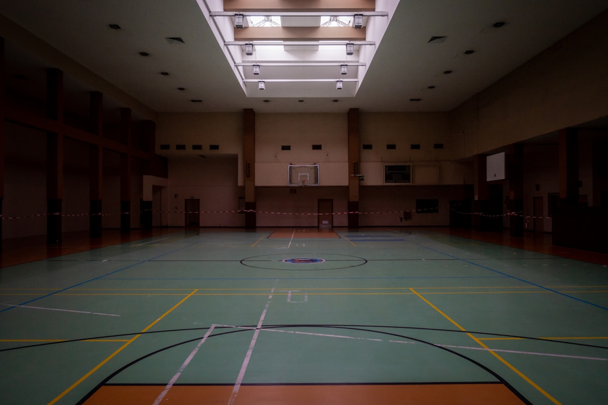 An empty school gym lit by a long skylight, its floor marked out for several sports.