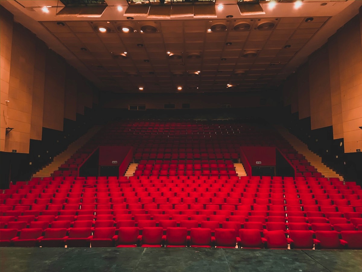 An empty auditorium seen from the stage, rows of red seats rising to the back wall.