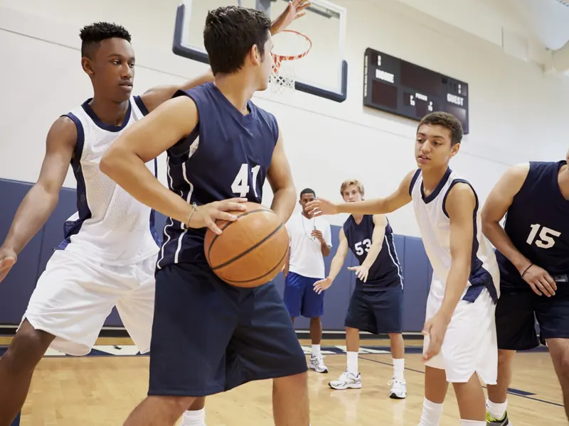 A high school basketball game in progress on a school gym floor.