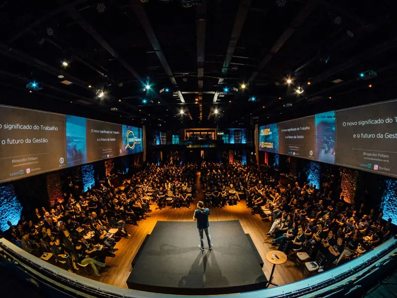 A hall filled with seated people facing a speaker on a low stage.