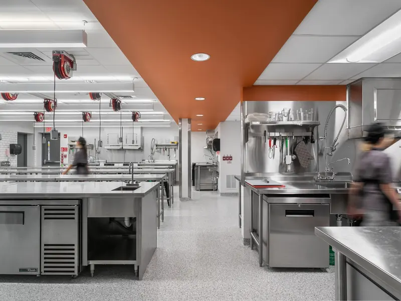 A commercial teaching kitchen with staff moving between stainless steel benches.