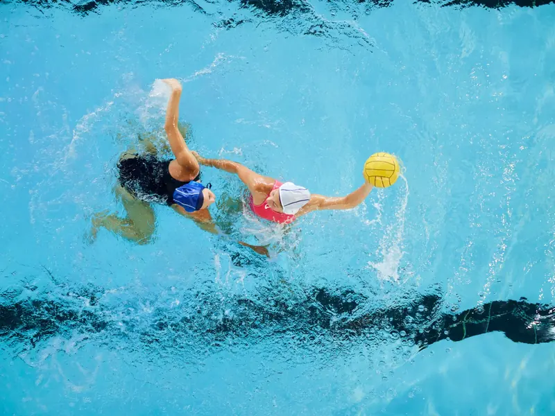 Two water polo players contesting the ball, seen from above the pool.